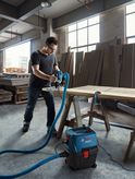Người sử dụng máy hút bụi bằng dụng cụ điện để hút gỗ trong xưởng.
