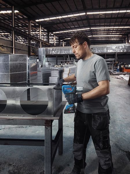 Một người mặc đồ bảo hộ đang khoan lỗ vào ống dẫn khí bằng kim loại trong một nhà máy.