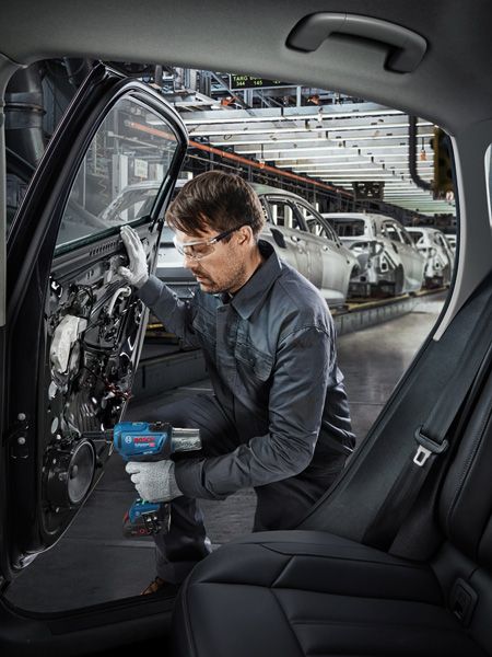 Một người mặc đồ bảo hộ đang sử dụng dụng cụ điện để lắp ráp cửa ô tô trong một nhà máy ô tô.