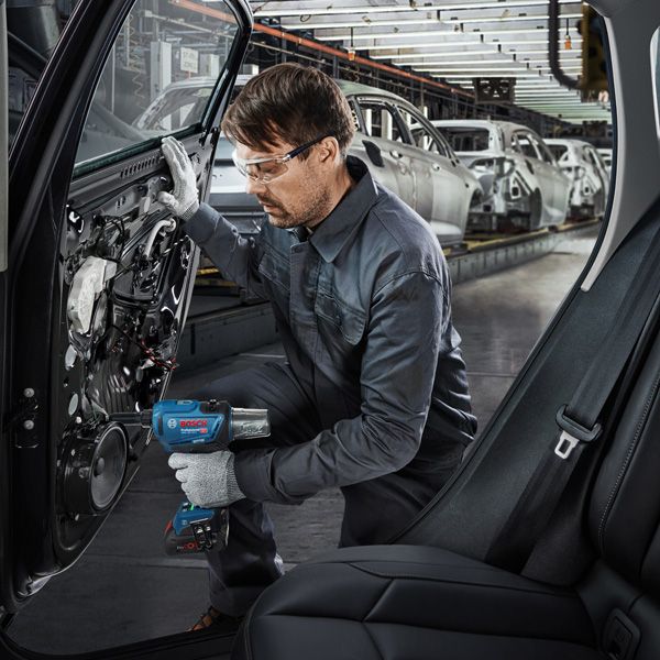 Một người mặc đồ bảo hộ đang sử dụng dụng cụ điện để lắp ráp cửa ô tô trong nhà máy.