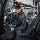 Một người mặc đồ bảo hộ đang sử dụng dụng cụ điện để lắp ráp cửa ô tô trong nhà máy.