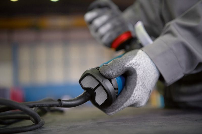 GWS 17-150 S Một người mặc đồ bảo hộ đang cầm một dụng cụ điện có dây trên bàn làm việc.