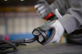 Một người mặc đồ bảo hộ đang cầm một dụng cụ điện có dây trên bàn làm việc.
