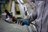 Một người mặc đồ bảo hộ đang cầm máy mài góc trong xưởng.