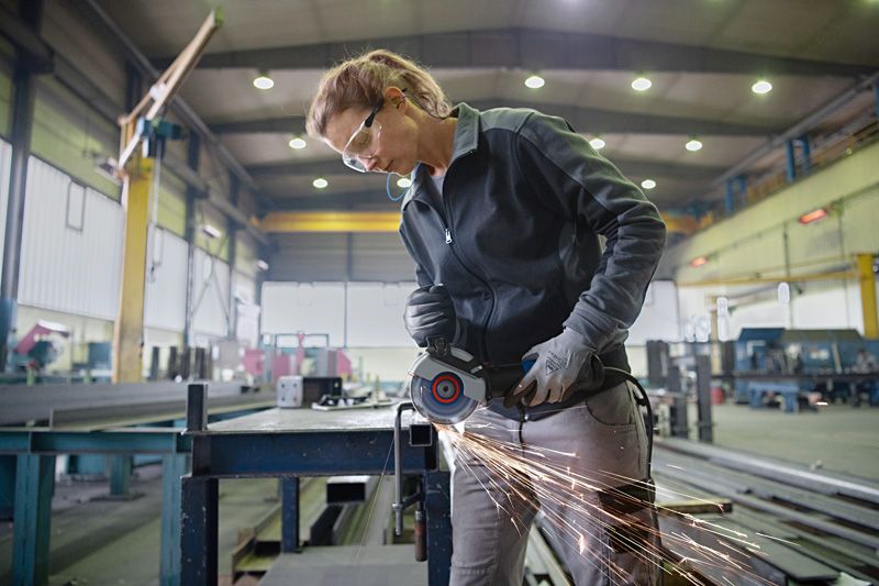 Một người mặc đồ bảo hộ đang mài kim loại trên bàn làm việc, tạo ra tia lửa.