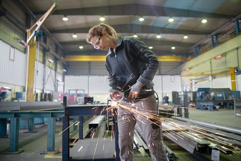 Một người mặc đồ bảo hộ đang sử dụng máy mài góc để cắt kim loại trong nhà máy.