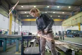 Một người mặc đồ bảo hộ đang sử dụng máy mài góc để cắt kim loại trong nhà máy.