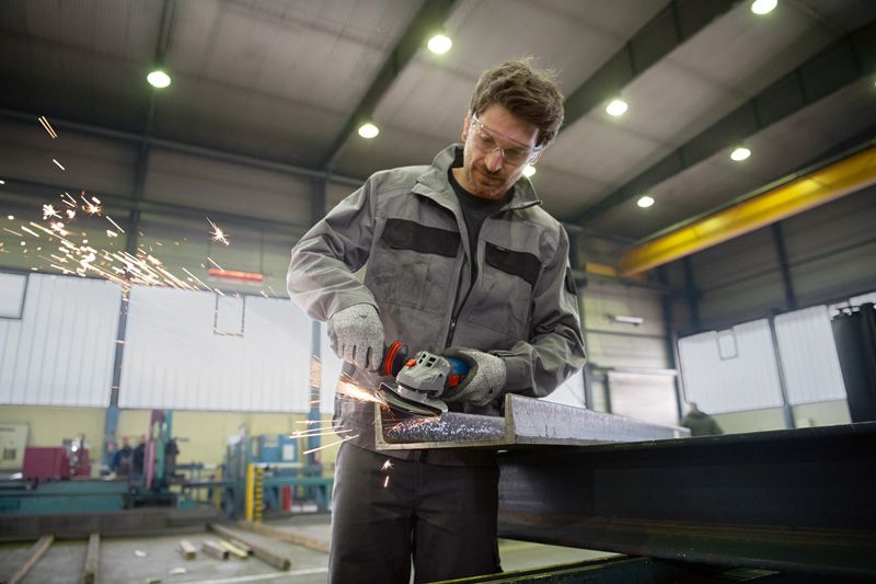 GWS 17-150 S Một người mặc đồ bảo hộ mài một thanh thép, tạo ra tia lửa bay.