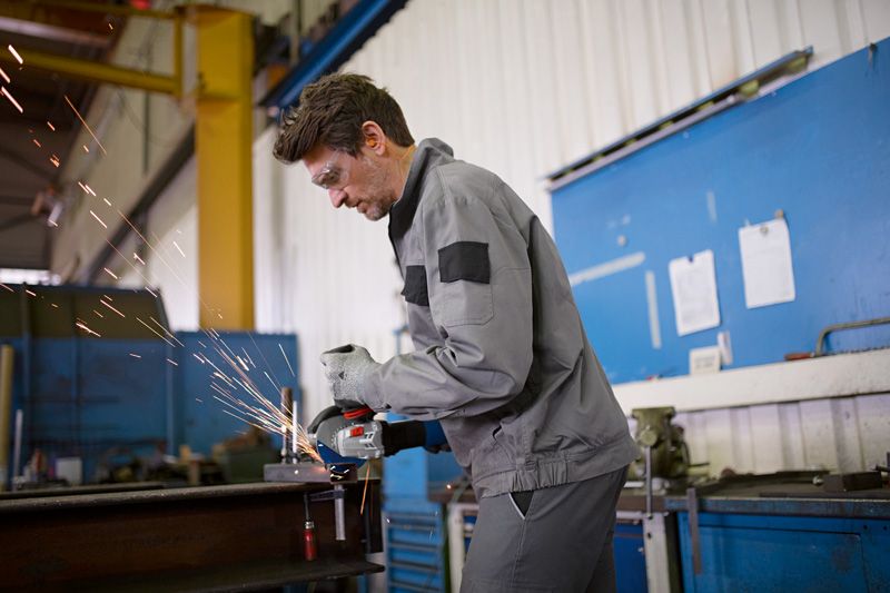 Một người mặc đồ bảo hộ đang mài kim loại, tạo ra tia lửa trong xưởng.