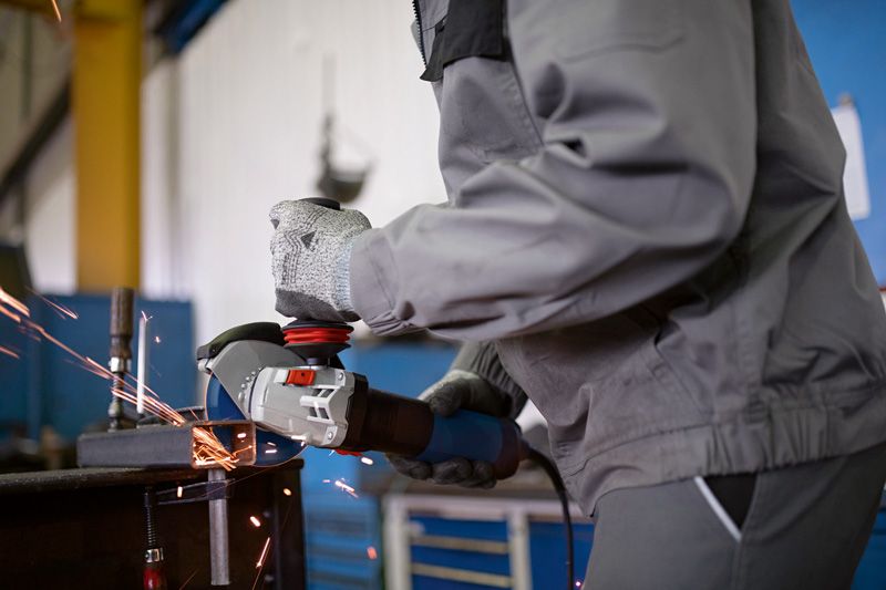 Một người mặc đồ bảo hộ đang mài kim loại, tạo ra tia lửa trong xưởng.