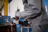 Một người mặc đồ bảo hộ đang mài kim loại, tạo ra tia lửa trong xưởng.