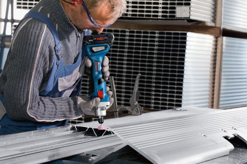 Một người đeo thiết bị an toàn đang mài một tấm kim loại bằng máy mài thẳng không dây.