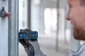 Người đeo thiết bị an toàn sử dụng máy đo laser để kiểm tra khoảng cách trên một thanh kim loại.