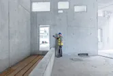Một người mặc thiết bị an toàn sử dụng máy đo laser trên bức tường bê tông.