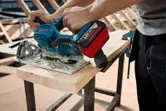 Người đang sử dụng máy cưa tròn không dây để cắt một tấm gỗ trên bàn làm việc.