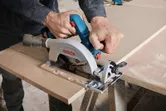 Một người đang cắt gỗ bằng máy cưa tròn không dây trên bàn làm việc.