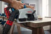 Một người cắt một tấm ván gỗ bằng một chiếc cưa tròn không dây được gắn vào một ống hút chân không.