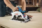 Một người đang cắt gỗ bằng máy cưa tròn không dây ở ngoài trời.