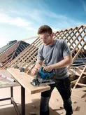 Một người mặc đồ bảo hộ đang cắt gỗ bằng máy cưa tròn không dây tại một công trường xây dựng.