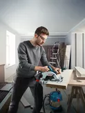 Người mặc đồ bảo hộ đang cắt gỗ bằng máy cưa tròn không dây trong xưởng.