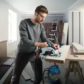 Một người mặc đồ bảo hộ đang cắt gỗ bằng máy cưa tròn không dây trong xưởng.