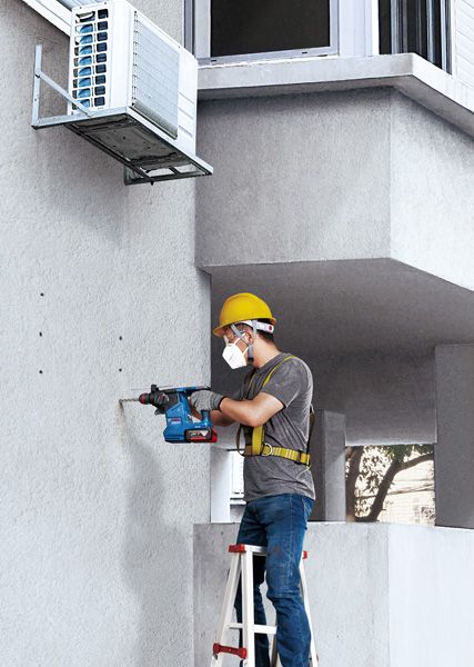 GBH 187-LI Một người mặc đồ bảo hộ đang khoan lỗ vào bức tường bê tông bên dưới máy điều hòa.
