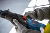 Người đeo thiết bị an toàn đang điều chỉnh dụng cụ điện bằng công tắc màu đỏ.