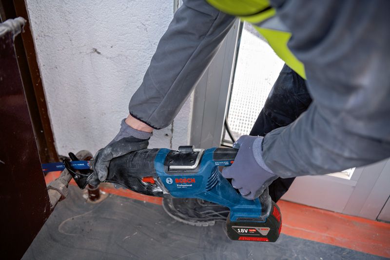 GSA 185-LI Một người mặc đồ bảo hộ đang sử dụng máy cưa lọng để cắt kim loại gần khung cửa.