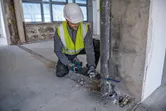 Một người mặc đồ bảo hộ đang sử dụng cưa lọng để cắt một ống kim loại.