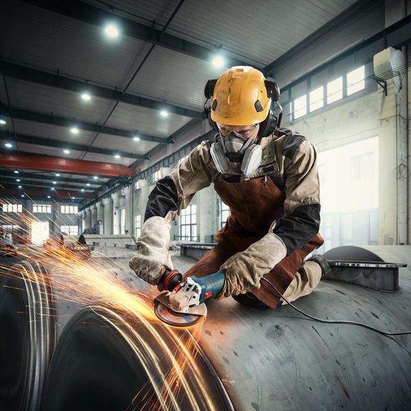 Một người mặc đồ bảo hộ đang mài kim loại, tạo ra tia lửa trong môi trường công nghiệp.