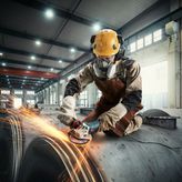 Một người mặc đồ bảo hộ đang mài kim loại, tạo ra tia lửa trong môi trường công nghiệp.