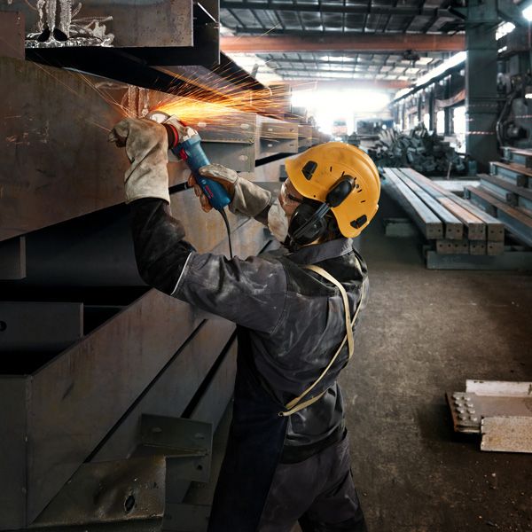 Một người mặc thiết bị an toàn mài một thanh kim loại, tạo ra tia lửa sáng.