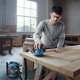 Một người mặc đồ bảo hộ đang chà nhám cửa gỗ bằng máy chà nhám quỹ đạo được kết nối.