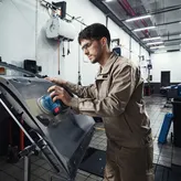 Một người mặc đồ bảo hộ đang chà nhám cửa ô tô bằng máy chà nhám điện.