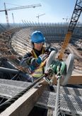 Một người mặc đồ bảo hộ đang sử dụng máy mài góc trên một thanh dầm thép tại công trường xây dựng sân vận động.