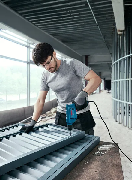 Người mặc đồ bảo hộ đang khoan vít vào khung kim loại tại công trường xây dựng.