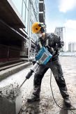 Một người mặc đồ bảo hộ đang vận hành máy phá dỡ để phá bê tông tại một công trường xây dựng.