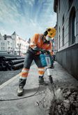 Một người mặc đồ bảo hộ đang phá vỡ vỉa hè bằng cầu dao điện trên đường phố thành phố.