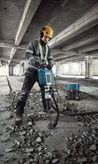 Một người mặc đồ bảo hộ đang sử dụng máy phá dỡ để phá sàn bê tông.