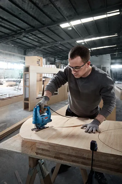 Người đeo thiết bị an toàn sử dụng máy cưa lọng để cắt các hình cong trên ván ép.