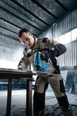 Một người mặc đồ bảo hộ đang vận hành máy cưa lọng để cắt một tấm kim loại.