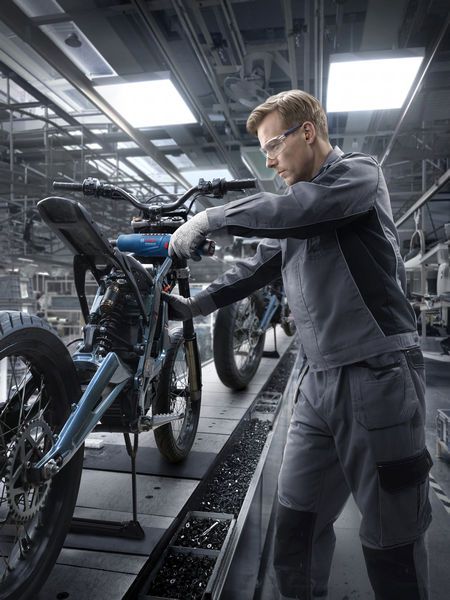 Một người mặc đồ bảo hộ đang lắp ráp khung xe máy trong nhà máy.