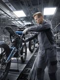 Một người mặc đồ bảo hộ đang lắp ráp khung xe máy trong nhà máy.