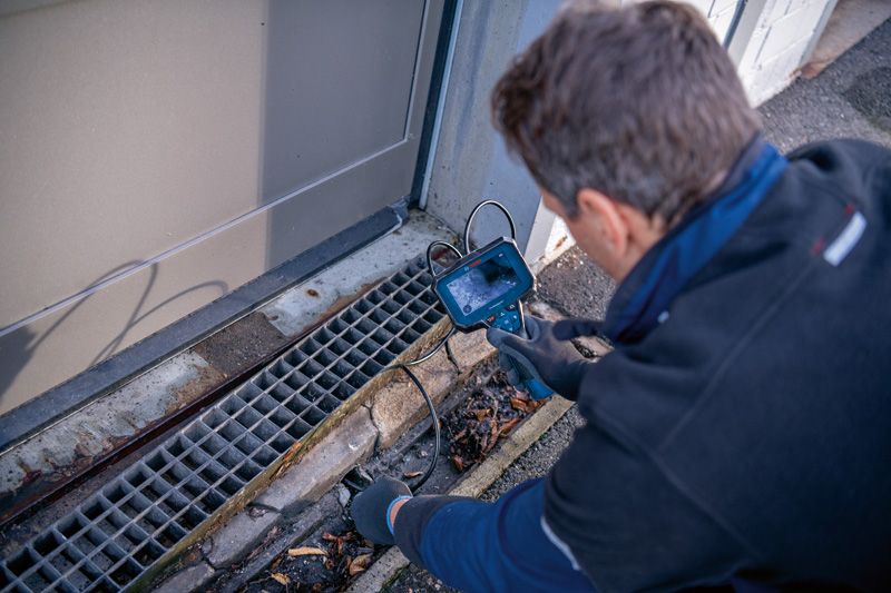 Một người mặc đồ bảo hộ đang kiểm tra cống thoát nước bằng camera kiểm tra.