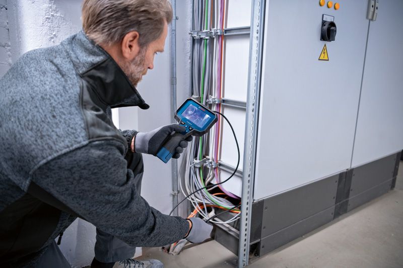 Một người mặc đồ bảo hộ đang kiểm tra hệ thống dây điện bằng camera kiểm tra.