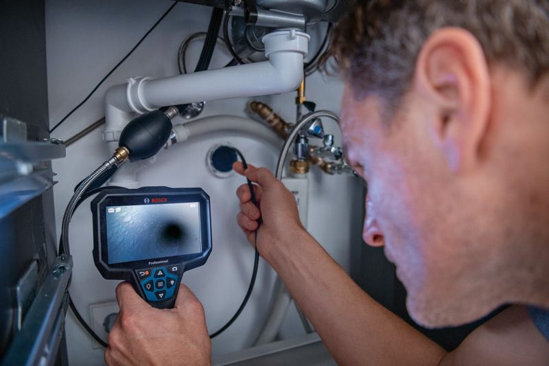GIC 5-27 C Một người đang kiểm tra hệ thống ống nước dưới bồn rửa bằng camera kiểm tra.