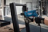 Một người mặc đồ bảo hộ đang khoan vào khung kim loại bằng máy khoan va đập.