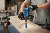 Một người mặc đồ bảo hộ đang khoan lỗ vào gỗ bằng máy khoan tác động.