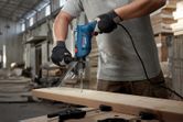Một người mặc đồ bảo hộ đang khoan vào tấm gỗ bằng máy khoan tác động.