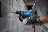 Một người mặc đồ bảo hộ đang khoan vào bức tường bê tông bằng máy khoan tác động.
